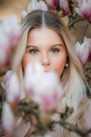 Junge Frau mit blonden Haaren, umgeben von magnolienblühenden Zweigen.