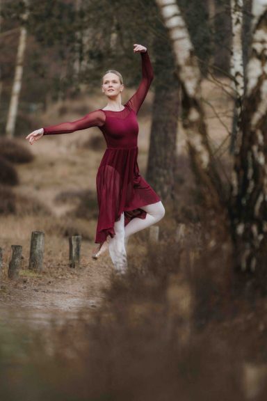 Tänzerin in rotem Kleid springt elegant durch eine herbstliche Waldlandschaft.
