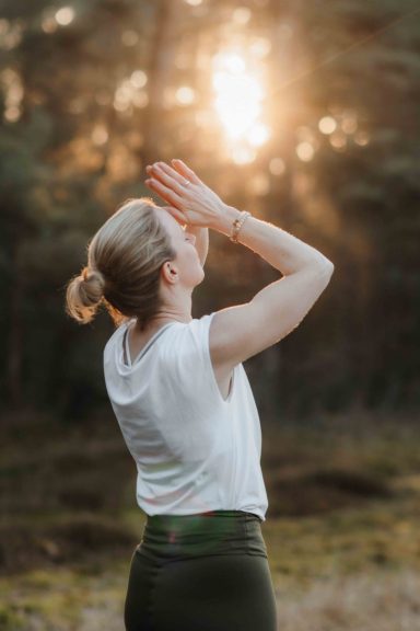 Frau im Freien, die die Hände zum Himmel hebt, umgeben von Sonnenstrahlen.