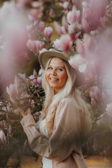 Blonde Frau in einem Hut, umgeben von blühenden Magnolien.