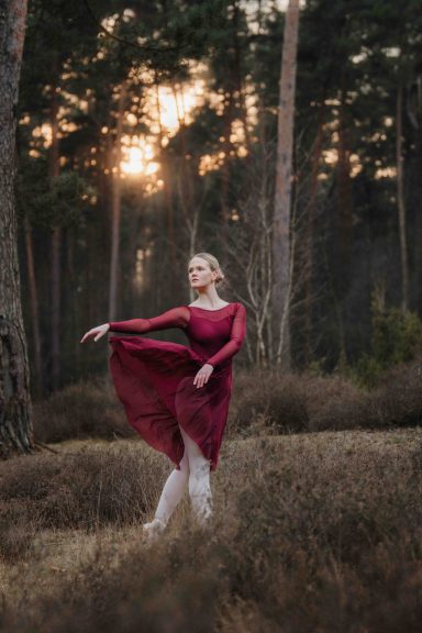 Frau in rotem Kleid tanzt in einer Waldlandschaft bei Sonnenuntergang.