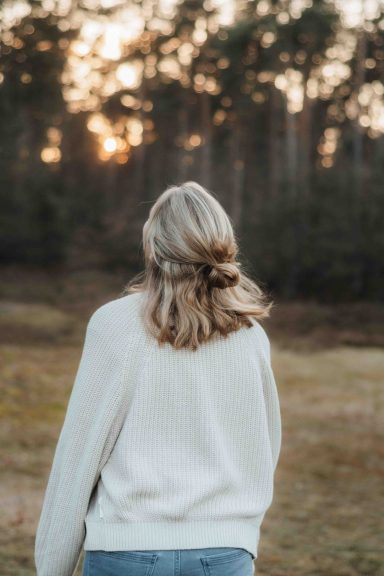 Eine Person mit blonden Haaren schaut in die Ferne, umgeben von Bäumen bei Sonnenuntergang.