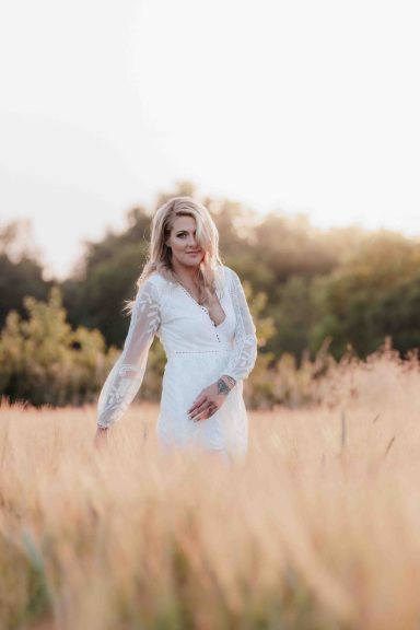 Eine Frau in einem weißen Kleid steht in einem Feld mit hohem Gras.
