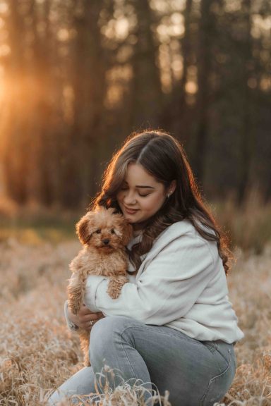 Junge Frau mit Hund sitzt in einem Feld bei Sonnenuntergang.