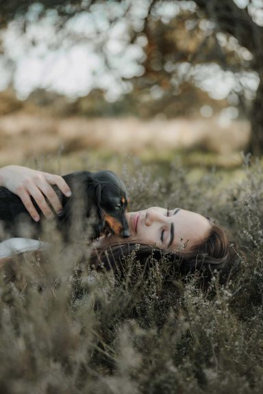 Frau liegt im Gras und kuschelt mit einem Hund.