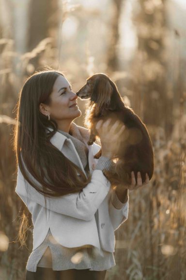 Eine Frau hält einen Hund in der Natur und lächelt ihm liebevoll zu.