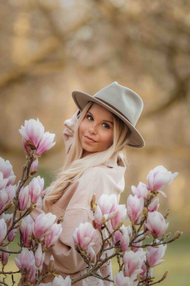 Frau mit blonden Haaren und Hut, umgeben von blühenden Magnolien.