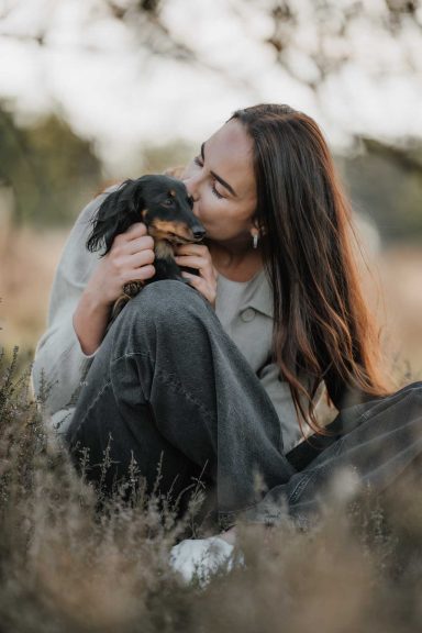 Eine Frau sitzt im Freien und umarmt einen kleinen Hund.