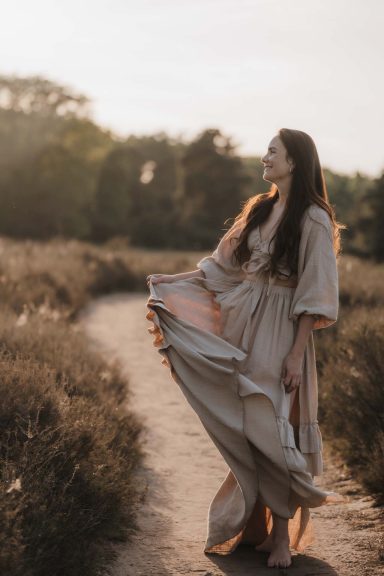 Eine Frau in einem fließenden Kleid läuft durch eine bewachsene Landschaft.