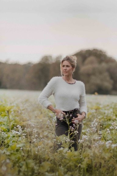 Frau steht in einem Feld mit Wildblumen und blickt nachdenklich in die Ferne.