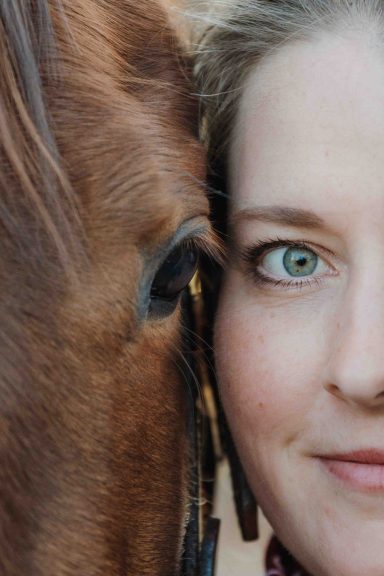 Frau mit einem Pferd, das eng an ihr Gesicht gedrückt ist, beide schauen zur Kamera.