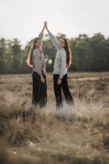 Zwei Frauen stehen auf einer Wiese und heben ihre Hände in die Luft.
